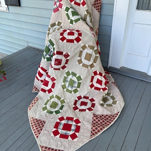 Op de afbeelding: Een vintage quilt met een patchwork ontwerp met rode, groene en witte vierkanten. De quilt is gemaakt van katoenen stof en heeft een vervaagde, antieke uitstraling.