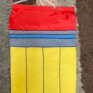 May include: A yellow pencil-shaped windsock with black lines and a red eraser. The windsock has a blue and gray stripe above the eraser.