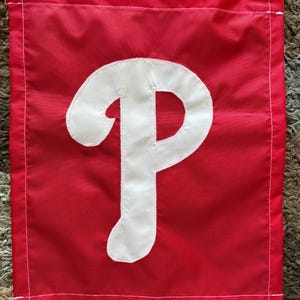 May include: A red flag with a white "P" logo. The flag is rectangular with a white stitched border and a white stitched outline around the letter. The flag is likely for outdoor use.