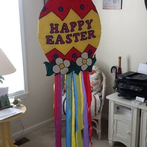 May include: A large, colorful Easter egg decoration with the words "HAPPY EASTER" in purple letters. The egg is red and yellow with blue dots, white flowers, and colorful ribbons hanging below.