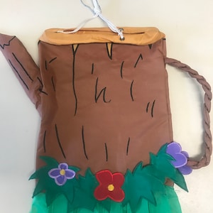 May include: A brown tree trunk shaped windsock with a green grass skirt and colorful flowers. The windsock has a loop at the top for hanging.