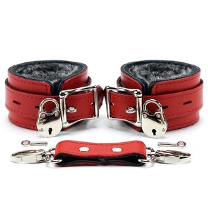 May include: Red leather and faux fur handcuffs with a silver lock and key. The handcuffs are connected by a red leather strap.