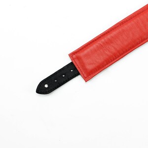 May include: A red leather collar with a black leather strap and silver buckle.