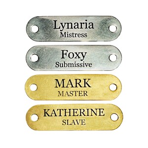 May include: Four metal dog tags with engraved text. Two tags are silver and two are gold. The silver tags read "Lynaria Mistress" and "Foxy Submissive". The gold tags read "MARK MASTER" and "KATHERINE SLAVE".