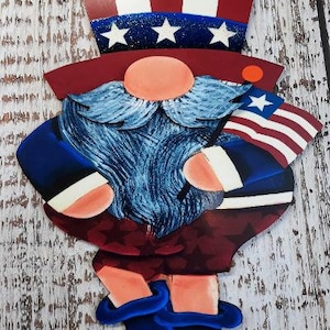 May include: A wooden gnome figurine painted in red, white, and blue with a stars and stripes hat, beard, and shorts. The gnome is holding a small American flag.