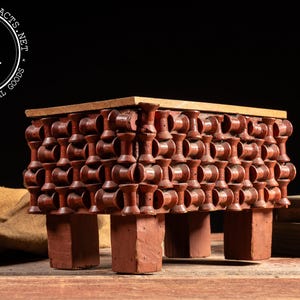 May include: A vintage, red-toned wooden table with a unique design. The table features a rectangular top and a decorative pattern of stacked, spool-like elements. The legs are square and sturdy, providing support. The table is a vintage industrial goods item.