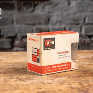 May include: A rectangular cardboard box for Cutler-Hammer compact oiltight pushbuttons. The box is white with red accents and black text. It features the CH Control logo, a graphic of a grid, and the text Compact Oiltight Pushbuttons.