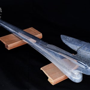 May include: A chrome-plated car hood ornament in the shape of a bird with outstretched wings. The ornament is resting on two wooden blocks.