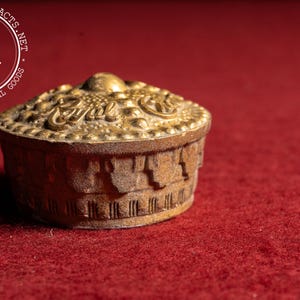 May include: A small, antique, gold-colored box with a domed lid. The lid is adorned with ornate detailing and the word "Royal". The box sits on a red surface, suggesting a vintage or collectible item.
