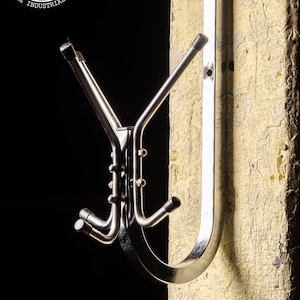 May include: A chrome coat rack with three hooks mounted on a wall. The rack is made of metal and has a simple, modern design.