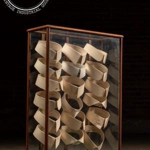 May include: A vintage display case with a wooden frame and glass panels. Inside, numerous cream-colored detachable shirt collars are neatly arranged. The case has a dark background and the text "INDUSTRIAL ARTIFACTS.NET" and "VINTAGE INDUSTRIAL GOODS".