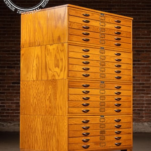 May include: A tall, light-brown wooden cabinet featuring four stacked sections, each containing five horizontal drawers. Each drawer is equipped with a dark, oval-shaped handle and a small metal label holder. The cabinet stands on four short, sturdy legs.