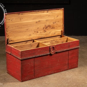 May include: A vintage red wooden storage chest with a hinged lid and three compartments inside. The chest has a worn, distressed finish and a metal latch.