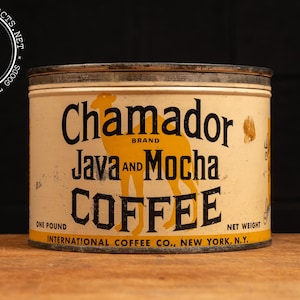 May include: A vintage one-pound tin can of Chamador brand Java and Mocha coffee. The can is yellow and white with a black and yellow illustration of a llama. The text on the can reads "Chamador Brand Java and Mocha Coffee, One Pound, Net Weight, International Coffee Co., New York, N.Y."