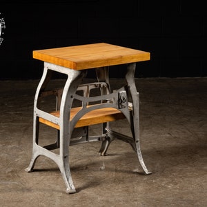 May include: A small, industrial-style table with a wooden top and a metal base. The table has two shelves and is painted a light gray color. The table is about 30 inches tall.