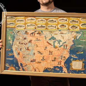 May include: Vintage framed map of the United States with illustrations of fish at the top. The map features colorful depictions of various activities and landmarks across the country, framed in a gold-colored wooden frame.