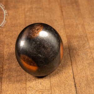 May include: A black and copper colored round knob with a smooth surface.