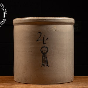 May include: A vintage white ceramic crock with a blue ribbon and the number "24" printed on the front.
