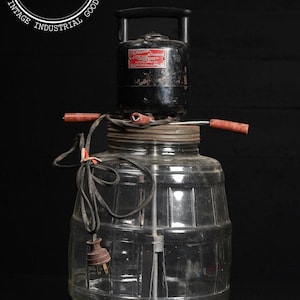 May include: Vintage glass jar with a black motor and red handles. The jar has a barrel-like design with horizontal ridges. The motor has a label that reads "Gemco Electric Standard". A power cord with a plug is attached.