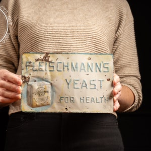 May include: Vintage metal sign advertising Fleischmann's Yeast for health. The sign is white with blue lettering and features a small image of a package of yeast.