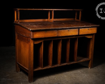 May include: A vintage wooden desk with a warm, brown finish. It features a raised back, two small drawers, and a series of vertical compartments below. The desk is designed for storage and organization, with a classic, antique aesthetic.