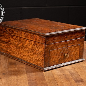 May include: A wooden box with a drawer. The box is made of dark wood with a grain pattern. The drawer has a brass knob. The box is sitting on a wooden surface.