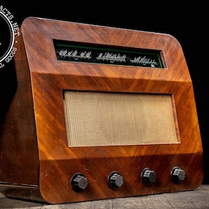 May include: Vintage wooden radio with a warm, reddish-brown finish and a textured speaker cover. The radio features a dark green display panel and four black knobs. The wood grain is visible, adding to its antique aesthetic.