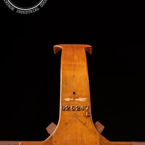 May include: A vintage wooden stand with a T-shaped top and a wide base. The stand is made of light brown wood and features the number "025247" stamped on the front. The stand is likely used for display or support.