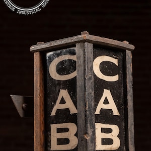 May include: Vintage wooden sign with the letters CAB, in white, on a black background. The sign is housed in a dark wooden frame with a metal lever on the side. The sign is from Industrial Artifacts.