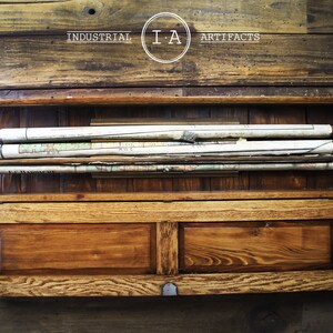 May include: A wooden cabinet with two drawers and a shelf. The shelf holds several rolled-up maps. The cabinet is labeled "INDUSTRIAL I.A ARTIFACTS".
