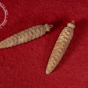 May include: Two antique, cone-shaped ornaments with a textured, ridged surface. The ornaments are a light brown color and have a small loop at the top. The background is a solid red.