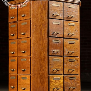 May include: A vintage, rotating wooden cabinet with numerous small drawers. The cabinet is made of light brown wood and features brass hardware on each drawer. The cabinet has a dark brown base and top, and the text "INDUSTRIAL ARTIFACTS" is visible.