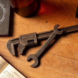May include: A vintage Ford USA adjustable wrench with a  rusted finish. The wrench is lying on a wooden surface with a second wrench.