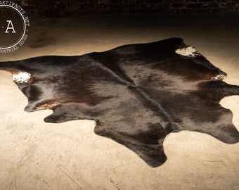 May include: A black and white cowhide rug with a natural, rustic look. The rug is made of real cowhide and has a unique, natural pattern. It is a great addition to any home decor.
