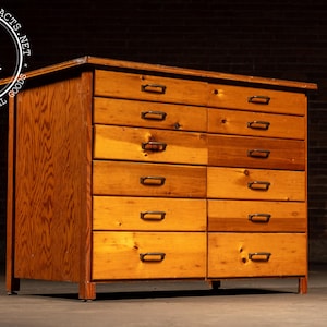 May include: A vintage wooden cabinet with multiple drawers. The cabinet is made of light-colored wood with a natural finish. Each drawer has a dark metal handle. The cabinet is rectangular and sits on short legs.