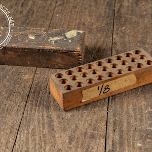 May include: Two vintage wooden boxes on a weathered wooden surface. One rectangular box is closed, while the other has multiple circular holes. The second box has a label with the number "1/8" on it. The boxes are likely for industrial use.