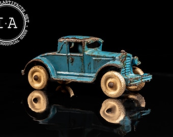 May include: A blue toy car with white tires and a black interior. The car is made of metal and has a vintage look. The car is sitting on a black surface.