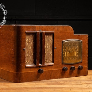 May include: A vintage wooden radio with a brown wood cabinet and a metal faceplate. The radio has a dial with numbers and a speaker grille. The radio is in good condition and has a classic look.