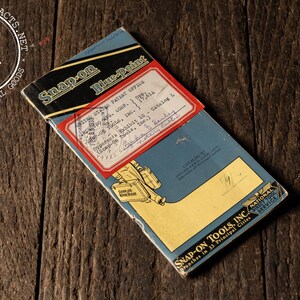 May include: Vintage Snap-on Blue-Point catalog on a wooden surface. The catalog is blue, black, and yellow with text and a red label. The Snap-on Tools Inc. logo is visible.