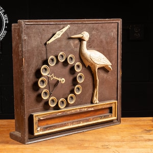 May include: A vintage wooden game with a clock face and a carved bird figure. The game has a series of round holes around the clock face and a small window at the bottom. The bird is perched on a wooden stand and has a small metal arm attached to it. The game is labeled "WOW WOW" on the arm.