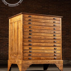 May include: A large, antique wooden cabinet with numerous drawers. The cabinet is made of light brown wood and features a rectangular shape with a flat top. Each drawer has a small, dark metal handle. The cabinet is supported by a sturdy base.