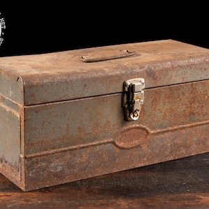 May include: A vintage metal toolbox with a rusted exterior and a silver latch. The toolbox has a handle on the top and a slightly curved design.