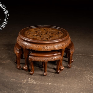 May include: A set of nesting tables with a dark brown finish. The largest table has a carved top and is surrounded by three smaller tables. The tables have ornate, curved legs and are likely made of wood.