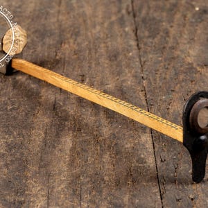 May include: A vintage wooden and metal tool with a ruler, a circular lens, and a handle. The tool has a light brown wooden ruler with black markings and a black metal frame. The tool is on a dark brown wooden surface.