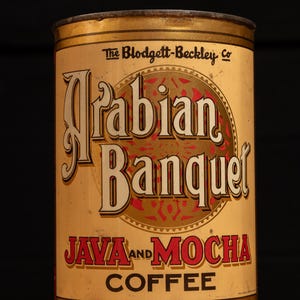 May include: A vintage tin can for Arabian Banquet Java and Mocha coffee. The can is gold with red and black lettering. The text on the can reads "The Blodgett-Beckley Co."