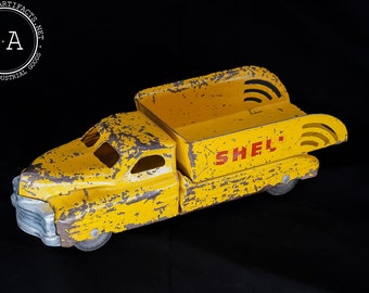 May include: Yellow toy dump truck with a Shell logo on the side. The truck is made of metal and has a worn, vintage look.