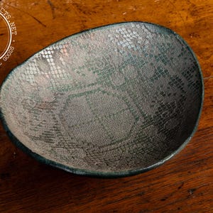 May include: A small, round, ceramic bowl with a blue glaze and a white, patterned design. The bowl is on a wooden surface.