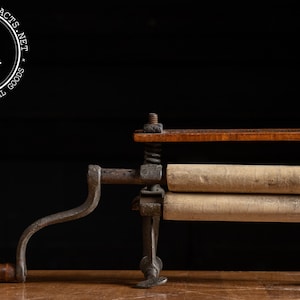 May include: Vintage clothes wringer with a wooden handle and rollers. The wringer has a cast iron frame and a wooden top. The rollers are made of a light-colored material. The wringer is designed to squeeze water from clothes.