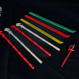 May include: Set of seven vintage cocktail picks, including four bamboo sticks with red, white, and yellow plastic animal heads, two red plastic swords, and one green plastic stick with the text "THE BIG MOUNTAIN - WHITEFISH MONTANA".