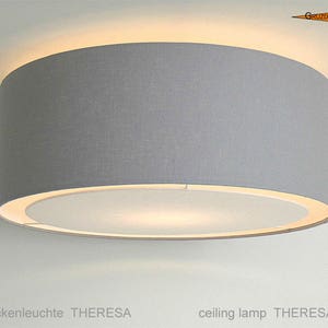 May include: A gray fabric ceiling lamp with a white inner shade. The lamp is round and has a simple design.